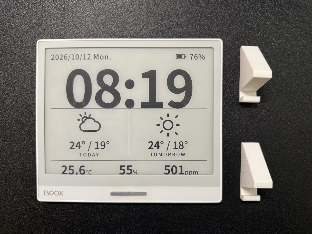 黒いデスクマットの上に置いた BOOX Leaf2。横向きの画面に日付、08:19、今日と明日の天気、25.6°C・55%・501ppm が出ている。右に 3D プリンターで作った白いスタンドの部品が 2 つ