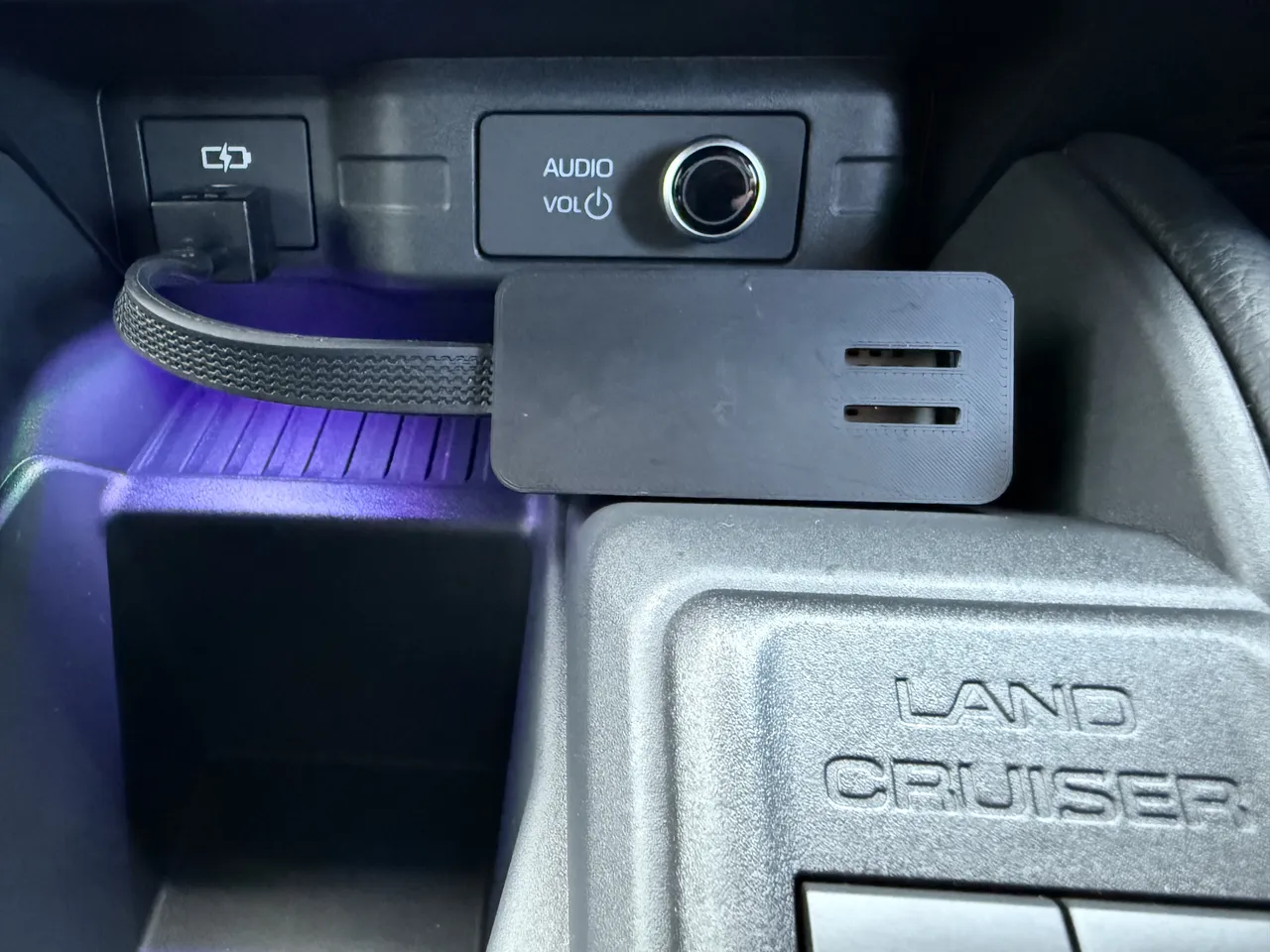 ランクル FJ のセンターコンソール。USB の差し込み口から編み込みのケーブルが出て、黒いケースに入れたセンサーが AUDIO のつまみの下に置いてある。右下に LAND CRUISER の刻印