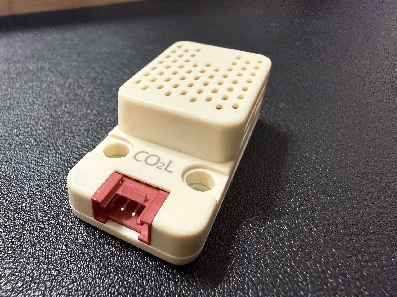 白い SCD41 ユニット。上面に通気の穴が並び、手前に赤い Grove の端子と「CO2L」の刻印がある