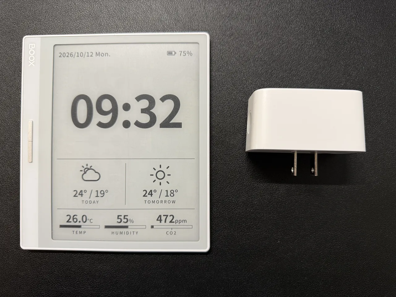 黒いデスクマットの上に並べた BOOX Leaf2 と SwitchBot プラグミニ。Leaf2 は縦向きで、画面に 09:32、今日と明日の天気、26.0°C・55%・472ppm、右上に電池の残量 75%。右の白いプラグミニは差し込み口の刃が見える向き